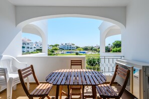 A balcony with a wooden table and chairs, overlooking a pool and buildings. - Casa Monteverde (Loulé)