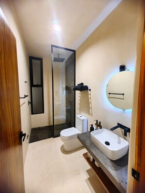 A modern bathroom with a glass shower enclosure, a white toilet, a vanity with a sink, and a mirror. - Koom Tulum, Your Perfect Getaway to Experience the Riviera Maya (Pet-Friendly) (Tulum)