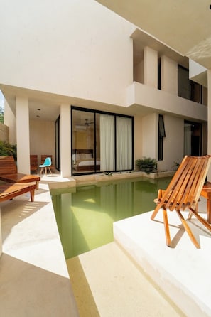 A modern building with a swimming pool, wooden lounge chairs, and a glass door leading to a room. - Koom Tulum, Your Perfect Getaway to Experience the Riviera Maya (Pet-Friendly) (Tulum)