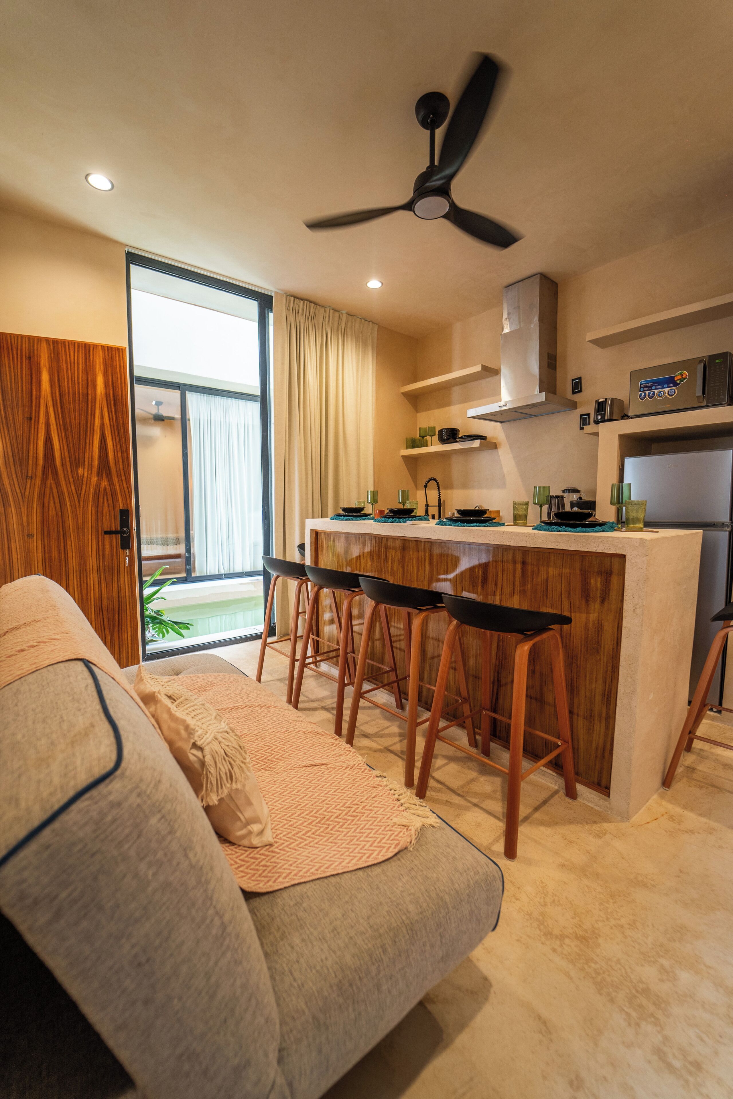 A modern kitchen with a central island, bar stools, and a ceiling fan.