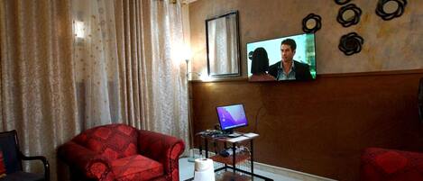 A living room with a red sofa, a glass coffee table, a TV mounted on the wall, and a computer on a small desk.