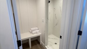 Moderni kylpyhuone, jossa on suihkukaappi, penkki pyyhkeille ja puulattia.