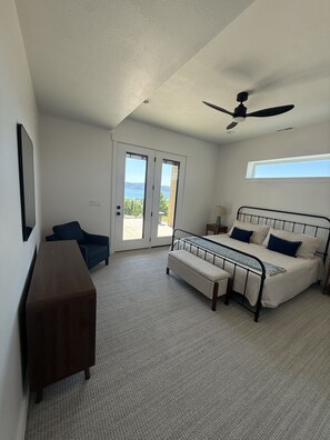 Ein Schlafzimmer mit einem Bett, einem Schreibtisch, einem Sessel und einem Deckenventilator, mit Blick ins Freie.