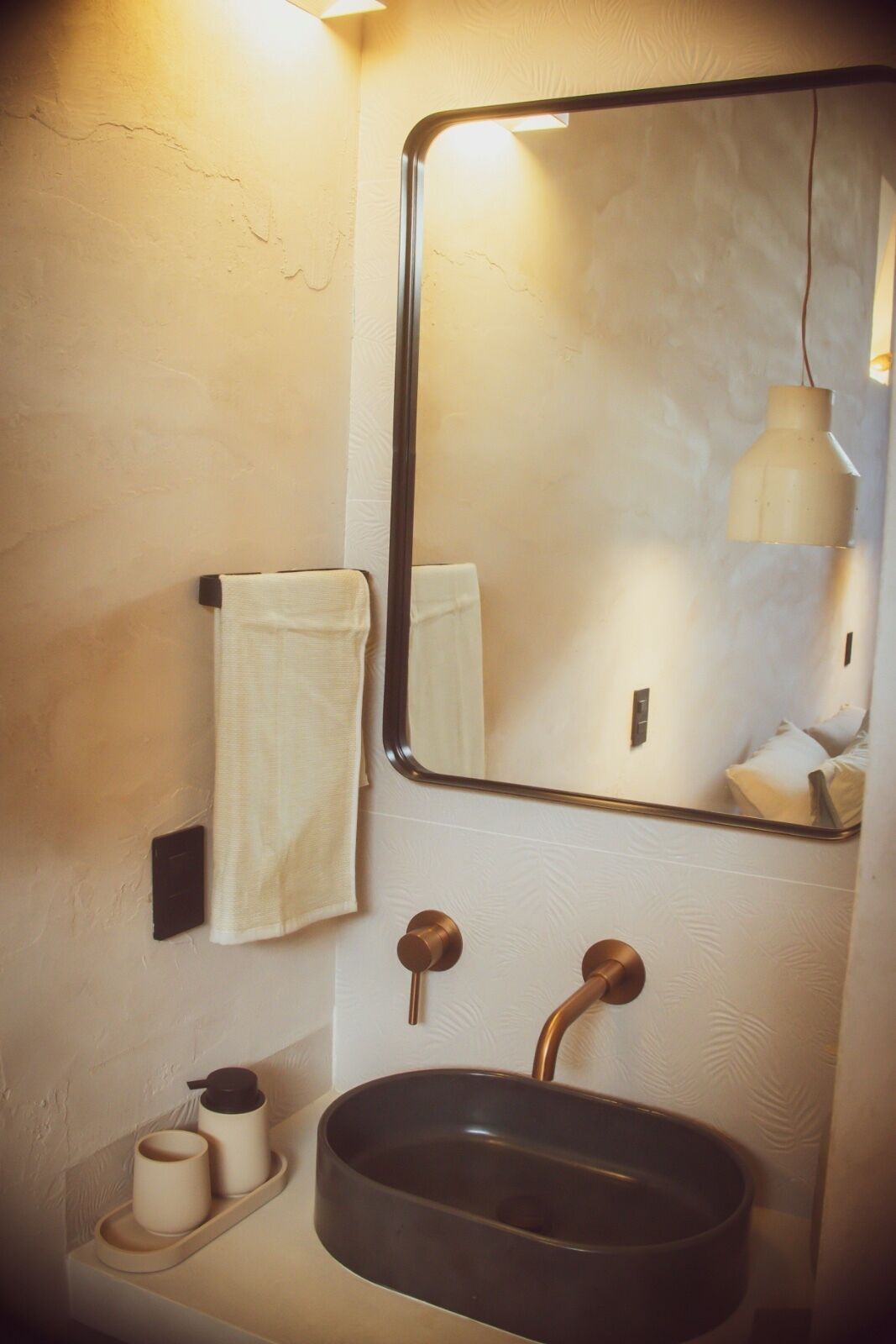 Een badkamer met een wastafel, spiegel, handdoekhouder en een klein plankje met toiletartikelen.