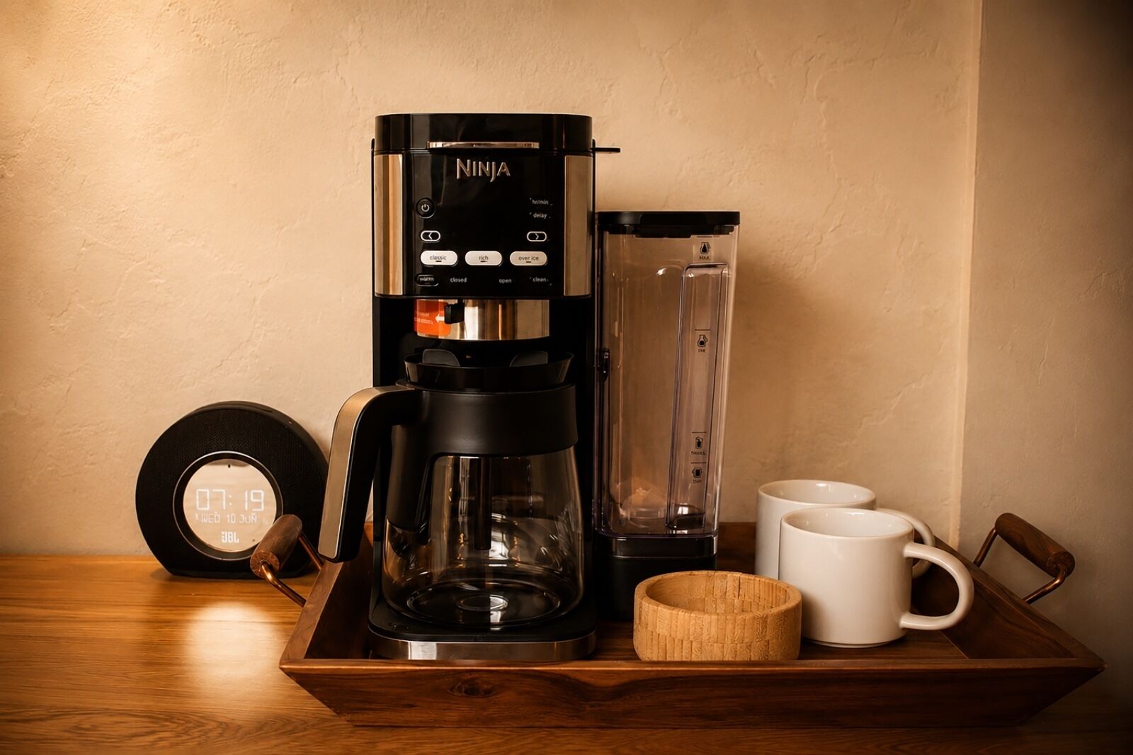 Una cafetera, un reloj y dos tazas sobre una bandeja de madera.