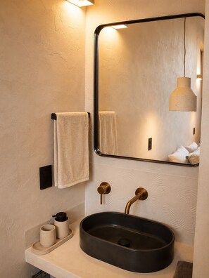 A bathroom with a round sink, two towel hooks, a mirror, and a pendant light. - Olivo Mío Apartment (La Paz)
