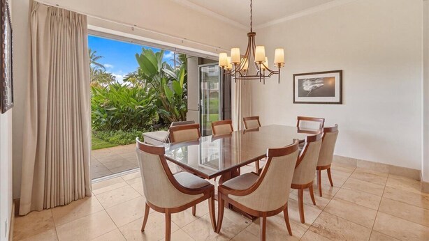 A dining area with a glass table, six chairs, a chandelier, and a view of greenery outside. - Dive into paradise at Honua Kai - Konea 102 (Lahaina)