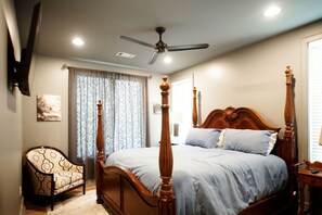 A four-poster bed with a ceiling fan, a chair with a patterned cushion, and a window with curtains. - Dancing Rabbit Grove (Oxford)