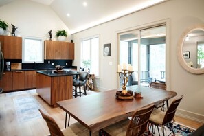 A modern kitchen with wooden cabinets, a central island, and a dining area with a wooden table and chairs. - Dancing Rabbit Grove (Oxford)