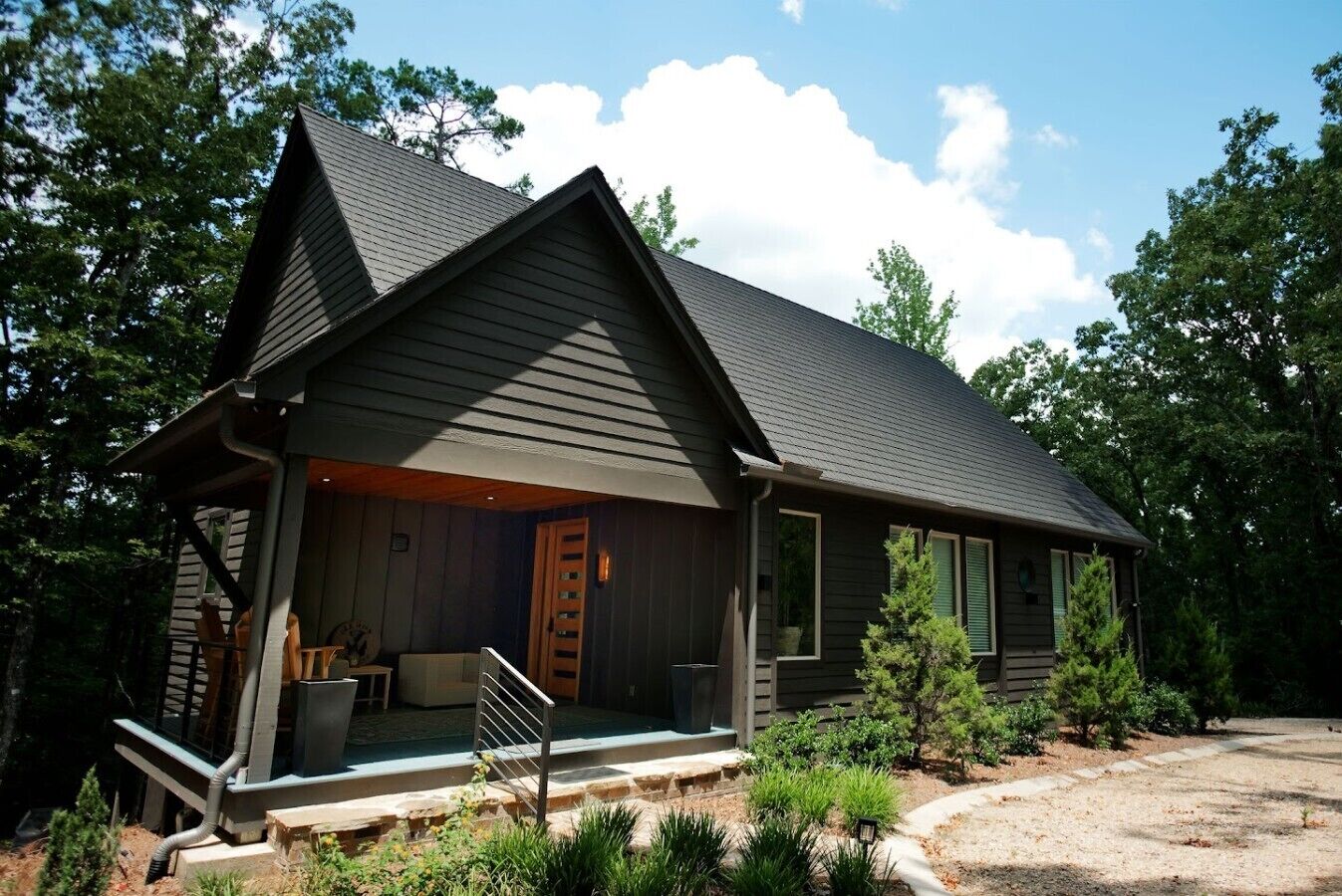 A two-story cabin with a porch, a covered outdoor seating area, and a small front yard.