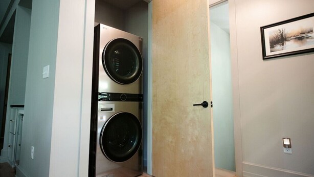 Une buanderie équipée d’un lave-linge et d’un sèche-linge doubles, d’une porte en bois et d’un tableau encadré accroché au mur.