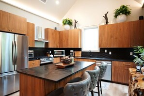A modern kitchen with wooden cabinets, stainless steel appliances, and a central island with bar stools. - Dancing Rabbit Grove (Oxford)