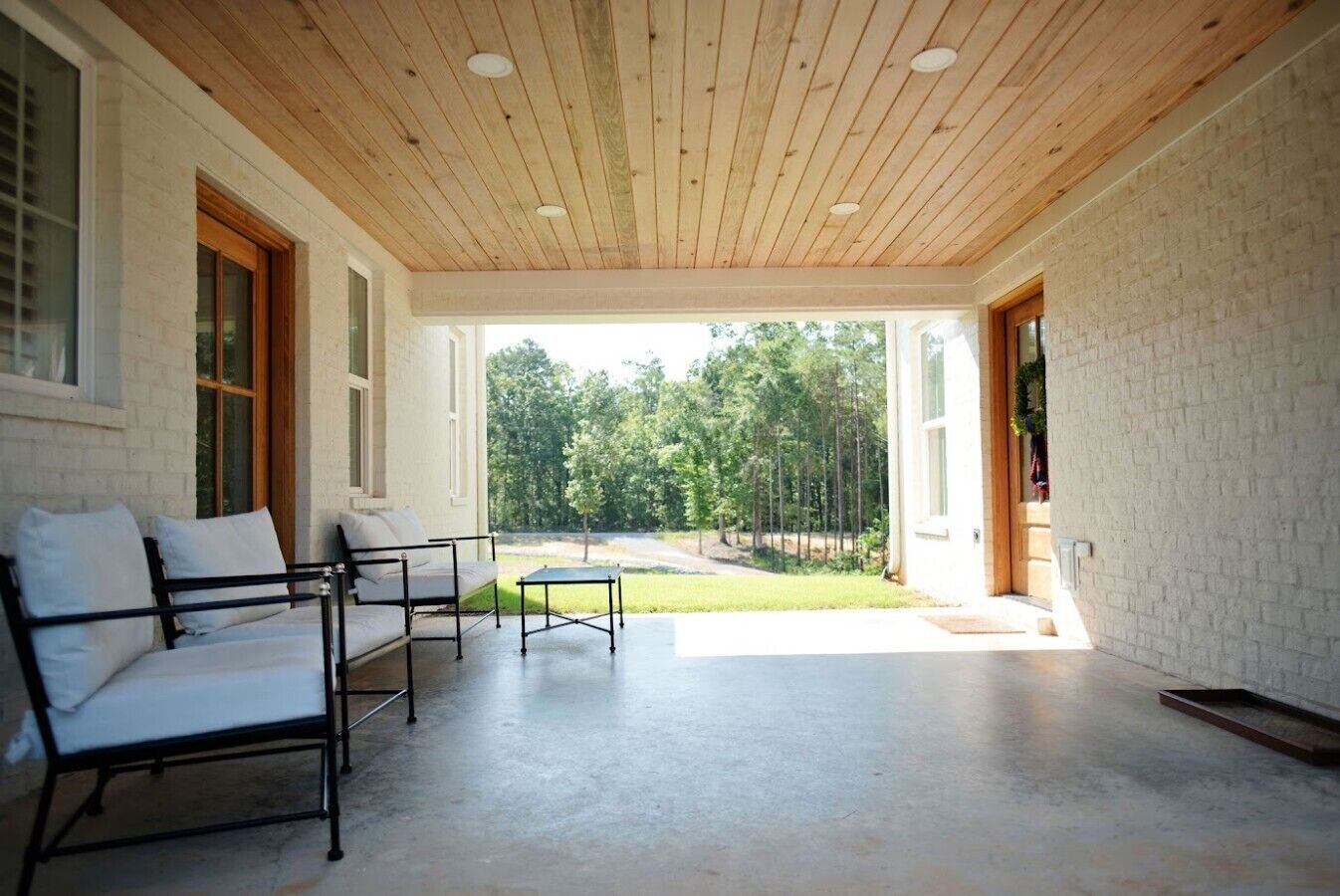 A covered patio with a sofa and table, a view of a green landscape, and a brick wall.