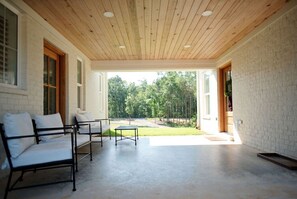 Un patio couvert avec un canapé et une table, une vue sur un paysage verdoyant et un mur en briques.