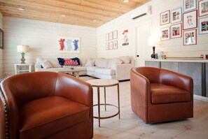 A cozy living room with two brown leather chairs, a small round table, a white sofa, and a decorative pillow with 'Miss' on it.