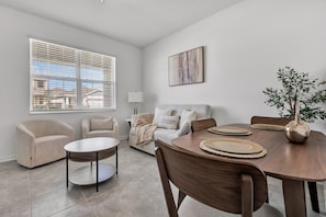 A modern living room with a dining table, two sofas, and a large window with blinds. - Modern 1BR | WiFi, Kitchen & Parking (Eagle Lake)