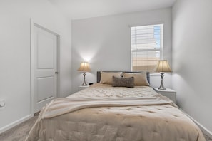 A bedroom with a bed, two bedside lamps, a window with blinds, and a door. - Modern 1BR | WiFi, Kitchen & Parking (Eagle Lake)