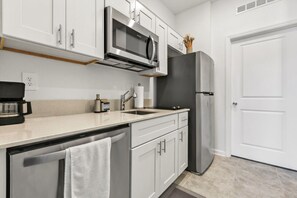 A modern kitchen with white cabinets, a stainless steel microwave, a refrigerator, and a coffee maker. - Modern 1BR | WiFi, Kitchen & Parking (Eagle Lake)