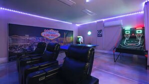 Une salle avec un néon, des jeux d’arcade et des fauteuils en cuir noir.