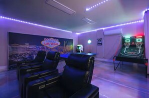 A room with a neon sign, gaming machines, and black leather chairs.