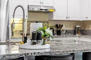 Eine Küche mit einer Arbeitsplatte aus Granit, einem modernen Wasserhahn und einem dekorativen Mittelstück mit Kerzen und Grünpflanzen.