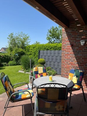 Une terrasse extérieure avec un mur en briques, une table ronde et des chaises colorées.