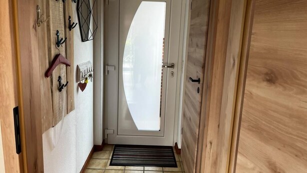 Um corredor com porta de madeira, cabide na parede e chão de azulejos.