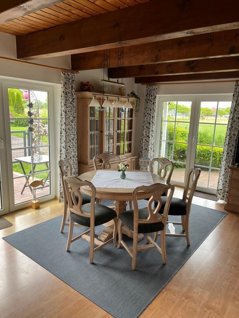 A dining area with a wooden table and chairs, a cabinet, and a view through large glass doors.