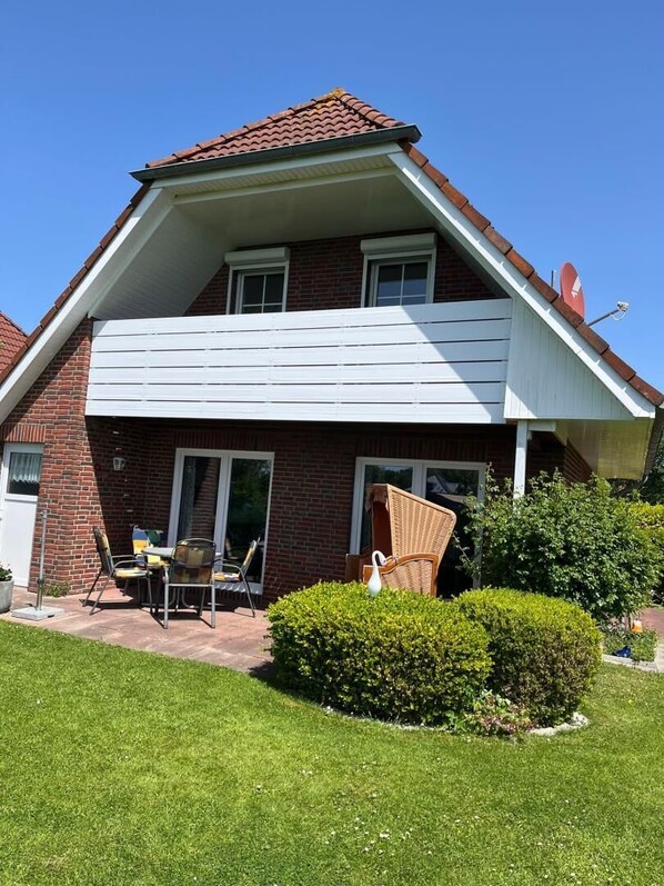Une maison à deux étages avec une façade en briques, un balcon agrémenté de meubles d’extérieur et un jardin bien entretenu.