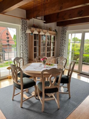 A dining area with a round table, six chairs, and a window with curtains. - NEW! Achterdeck Vacation Home (Hooksiel)