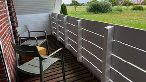 Uma varanda com piso de madeira, cadeiras de metal e corrimão branco.