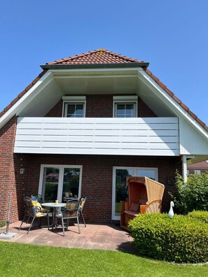 Une maison à deux étages, avec une façade en briques, un porche blanc et un petit patio aménagé avec du mobilier d’extérieur.