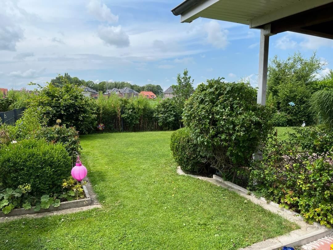 Een verzorgde tuin met gazon, verschillende struiken en een roze lantaarn.