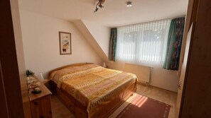 Een slaapkamer met een bed, een radiator, een raam met gordijnen en een foto aan de muur.