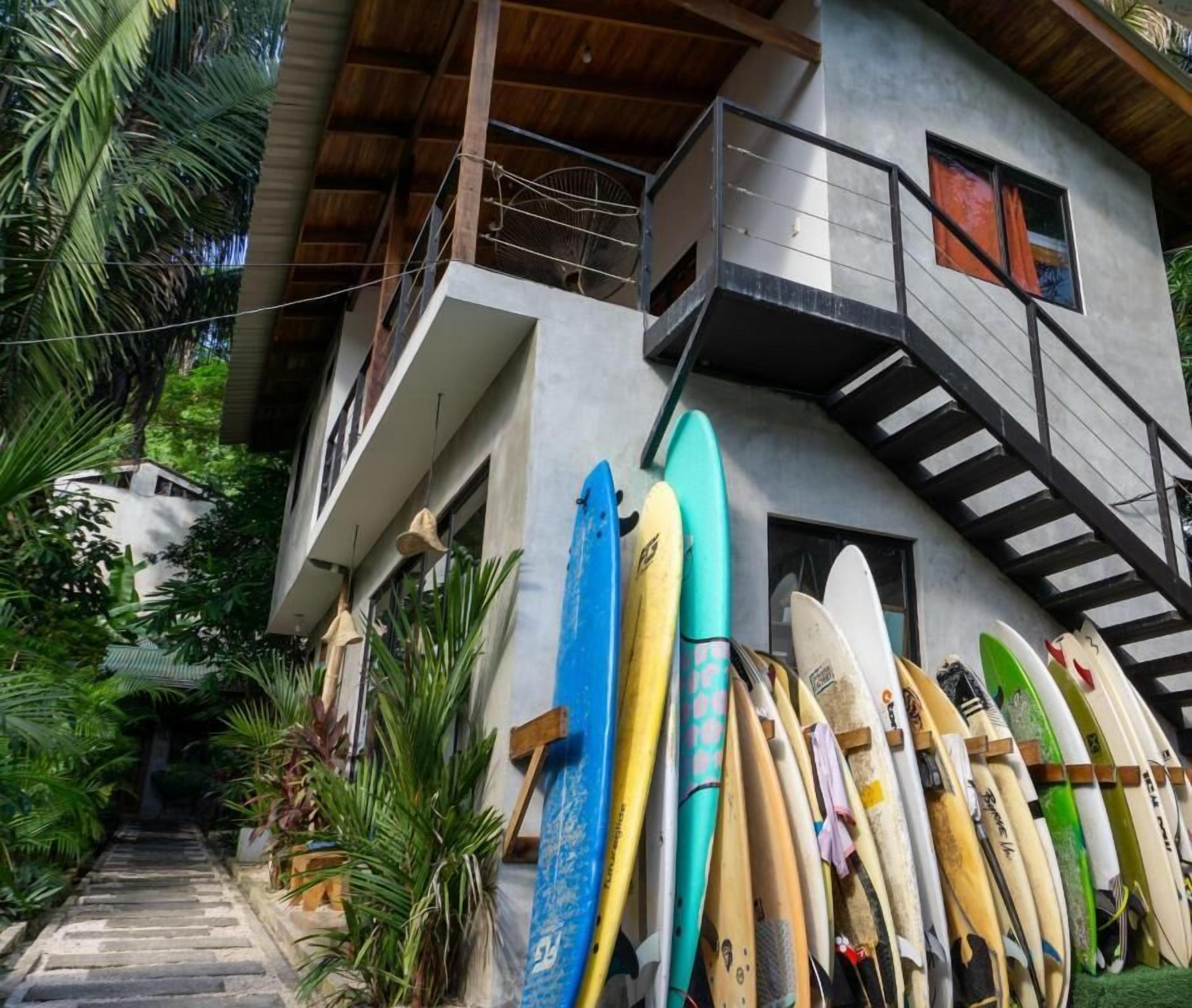 A building with a staircase leading to a balcony, surrounded by various surfboards.