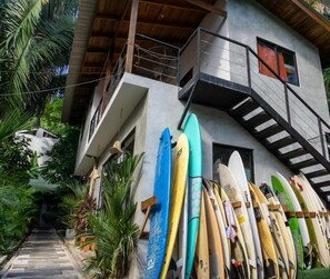 A building with a staircase leading to a balcony, surrounded by various surfboards. - Cabinas Playa Surf Hostel (Cobano)