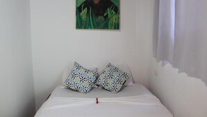 A bedroom with a bed, two patterned pillows, a wall-mounted painting, and a curtain. - Cabinas Playa Surf Hostel (Cobano)