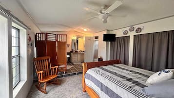 A bedroom with a bed, a rocking chair, a desk, and a television.