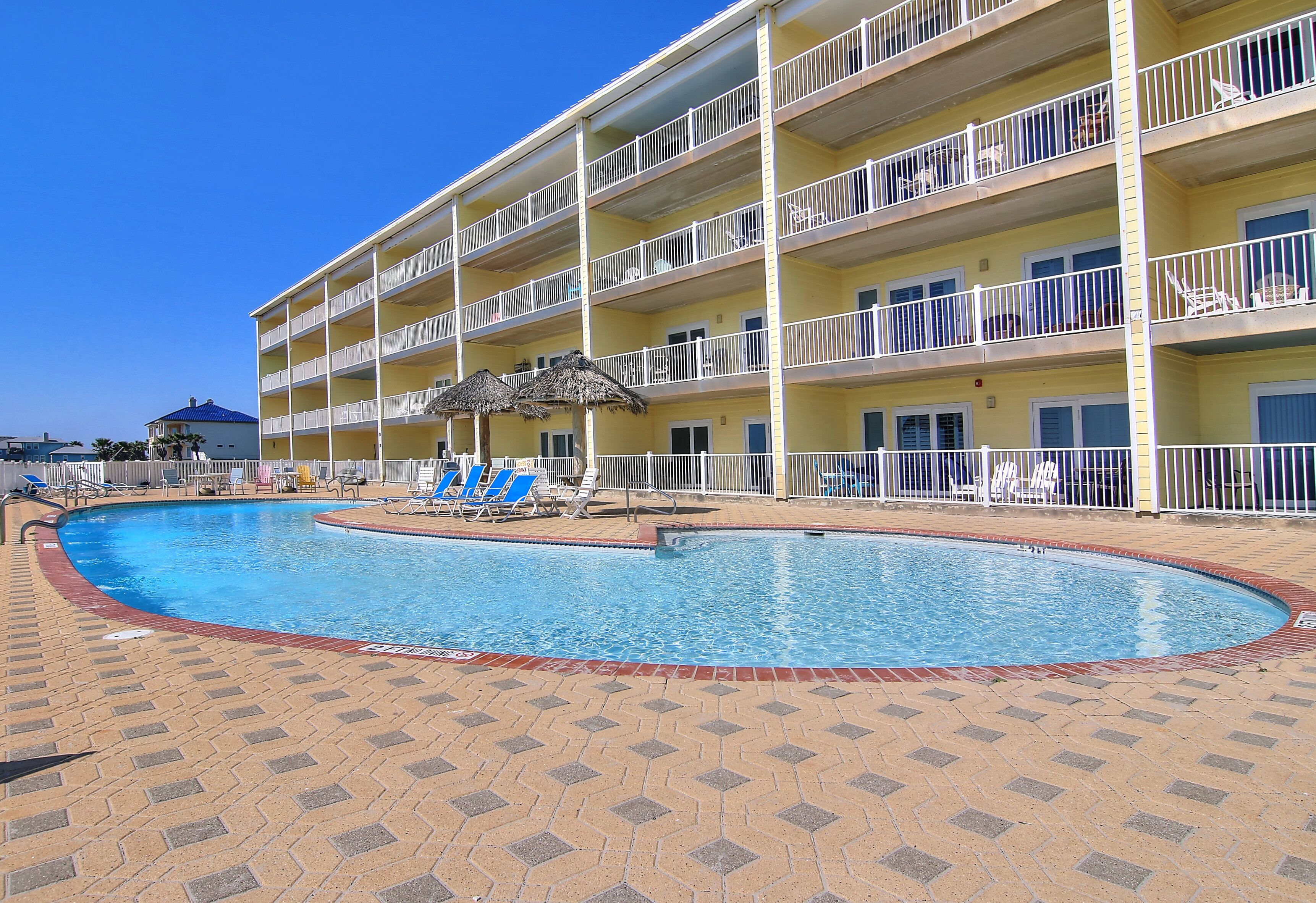A hotel with a swimming pool, multiple balconies, and lounge chairs.