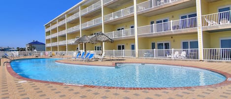 A hotel with a swimming pool, multiple balconies, and lounge chairs.