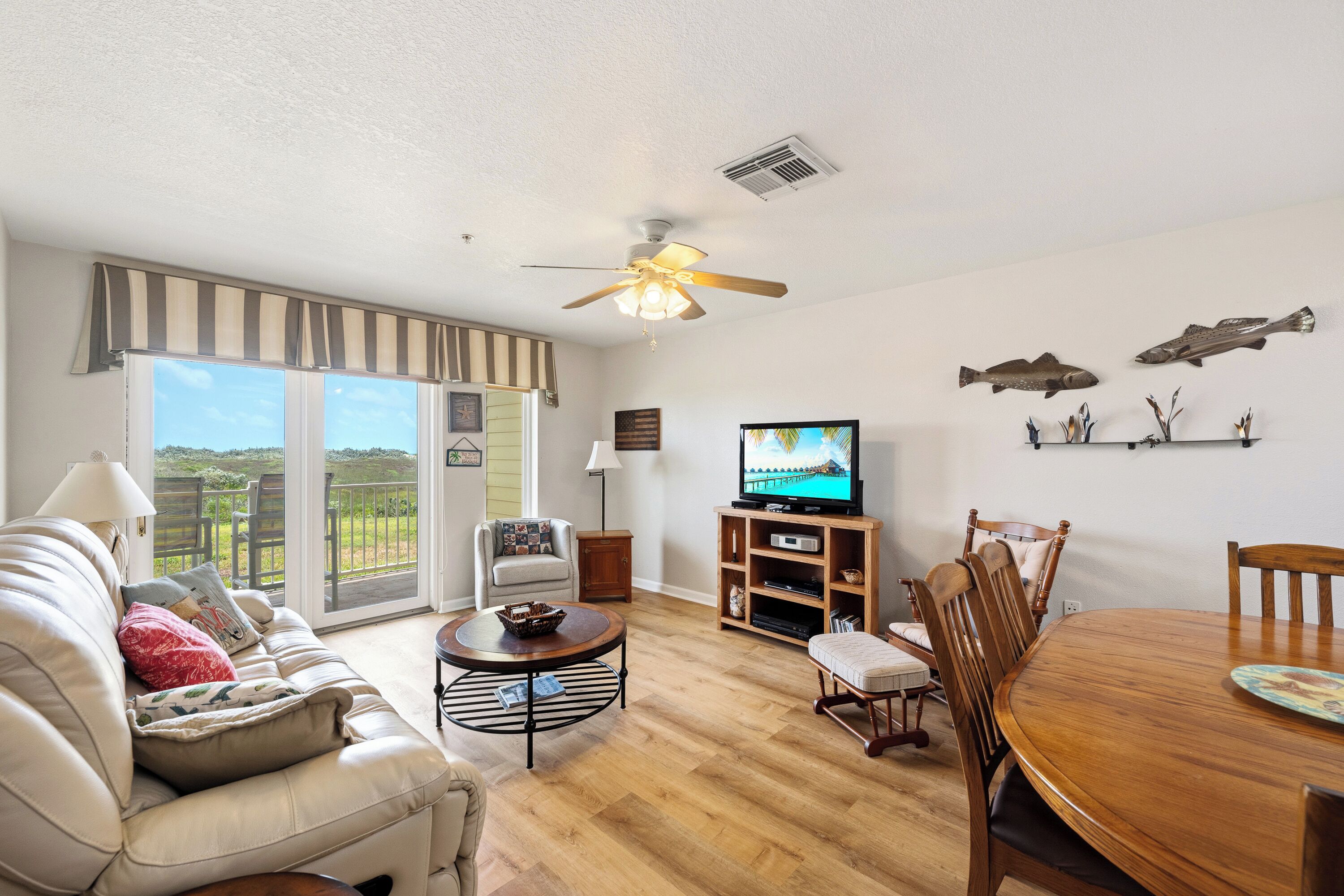A living room with a sofa, a television, a wooden dining table, and a ceiling fan.