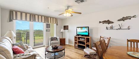 A living room with a sofa, a television, a wooden dining table, and a ceiling fan.