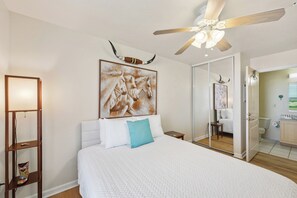 A bedroom with a large bed, a ceiling fan, a painting of horses, a mirror, and a wooden floor. - Coastal Retreat with Pool & Beach Access (Port Aransas)