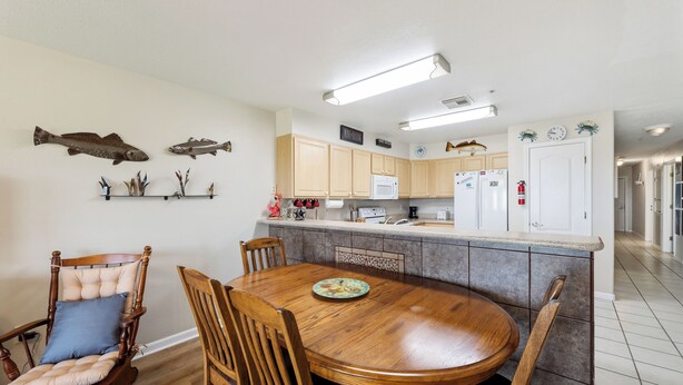 A kitchen with wooden cabinets, a dining table with chairs, and decorative fish on the wall. - Coastal Retreat with Pool & Beach Access (Port Aransas)