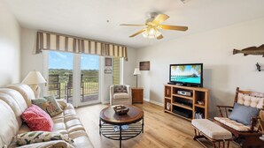 A living room with a sofa, a television, a wooden coffee table, and a ceiling fan. - Coastal Retreat with Pool & Beach Access (Port Aransas)