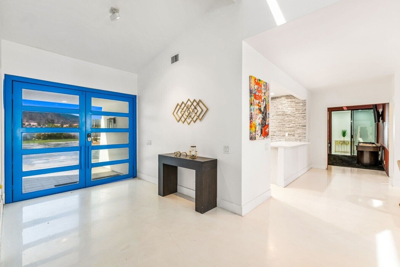 A spacious hallway with a blue door, a console table, and a wall-mounted decorative piece.