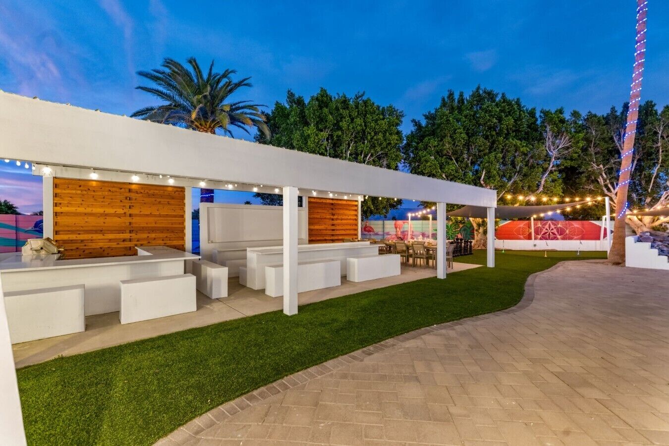 An outdoor patio area with a white pergola, seating, and a grassy lawn.