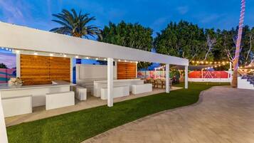 An outdoor patio area with a white pergola, seating, and a grassy lawn.