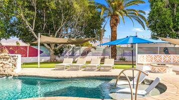 A swimming pool with lounge chairs and a fire pit area.