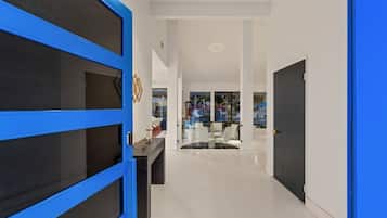 Un corridoio con una porta blu, un divisorio in vetro e una sala da pranzo con sedie bianche e un tavolo.